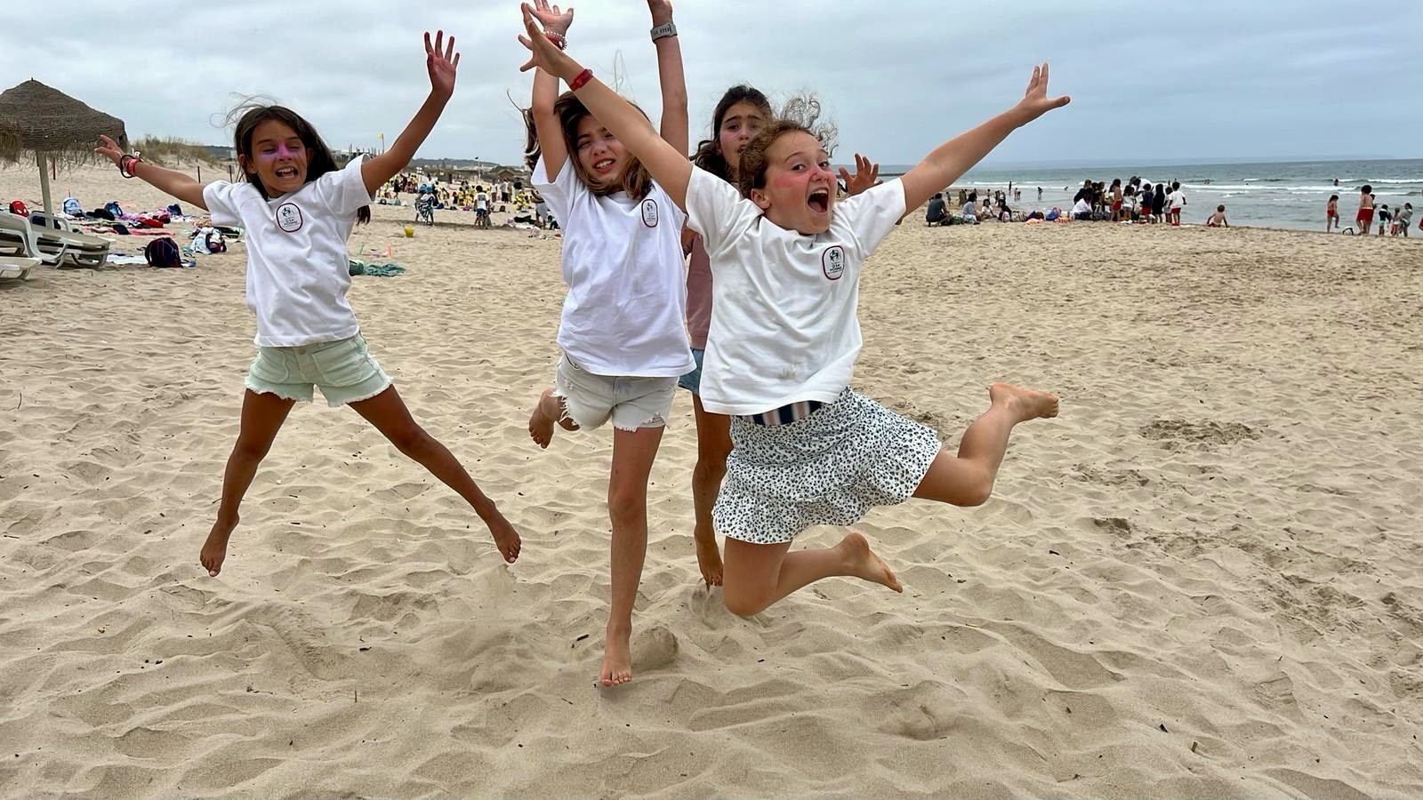 Crianças com t-shirts da escola a saltar na praia