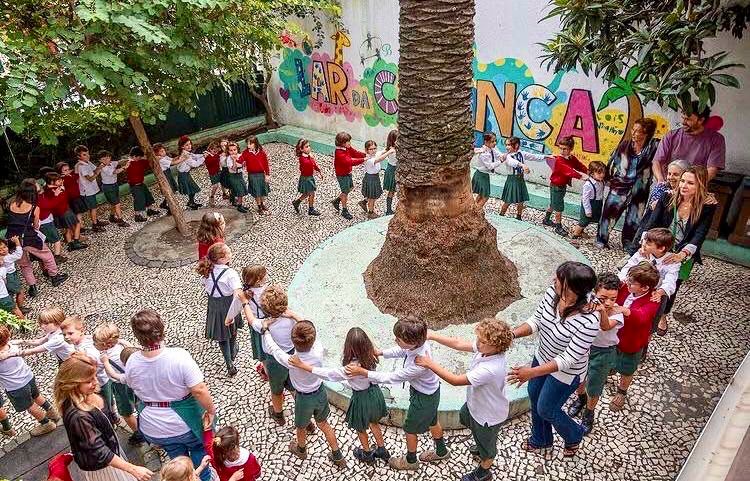 Children in a circle in the schoolyard next to the palm tree