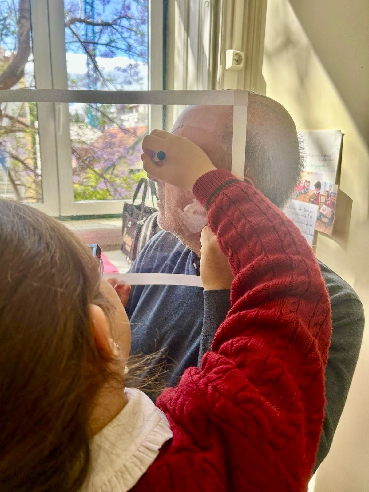 Child drawing on a glass pane with a jacaranda tree in bloom in the background