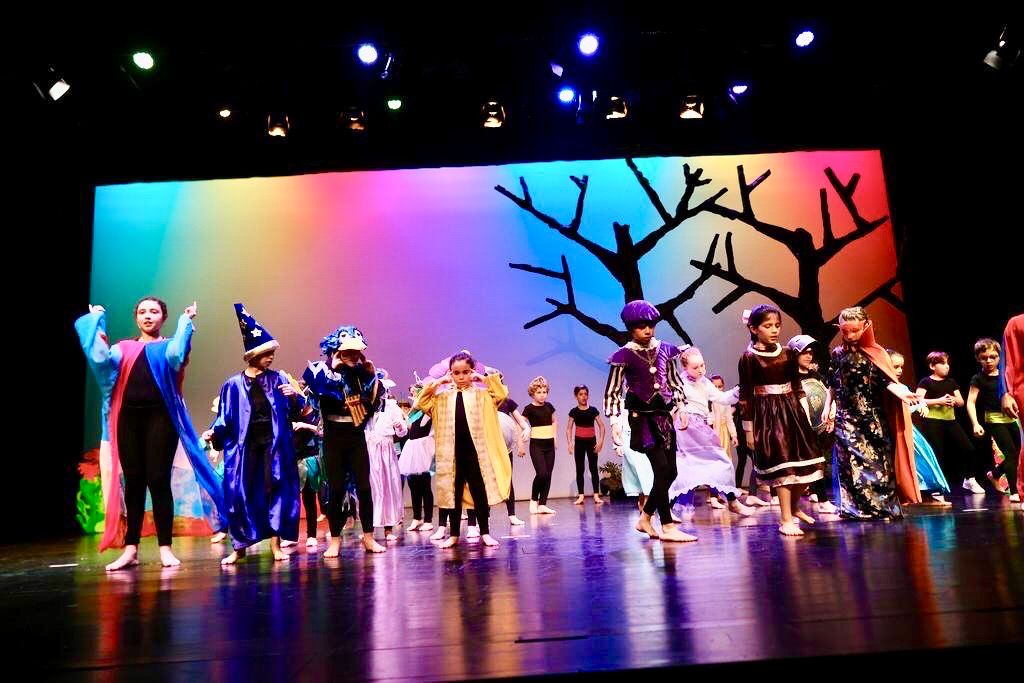 Pupils in a theatre play on stage with colourful scenery